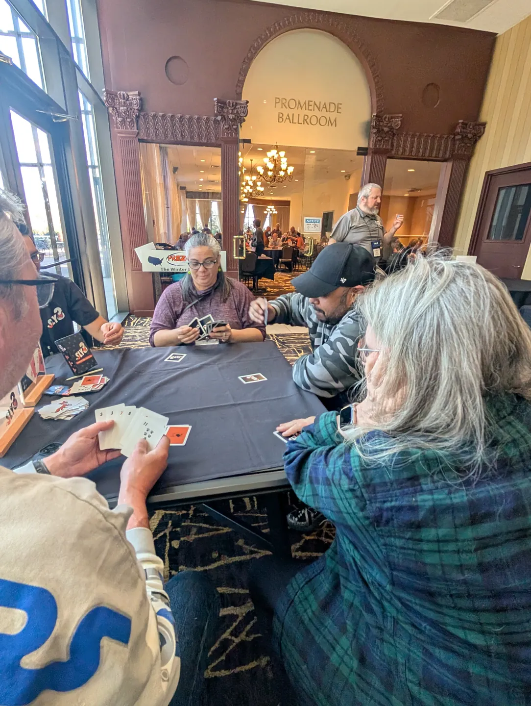 Five players around a table mid-round with Sly3 cards spread across it