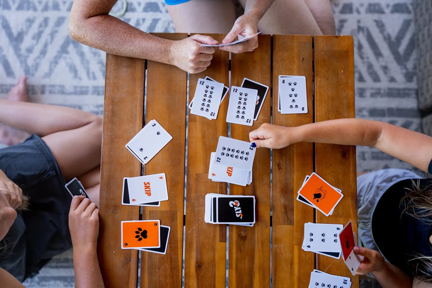 Overhead view of a Sly3 round on a wooden table, face-up cards in front of each player and a pile in the middle